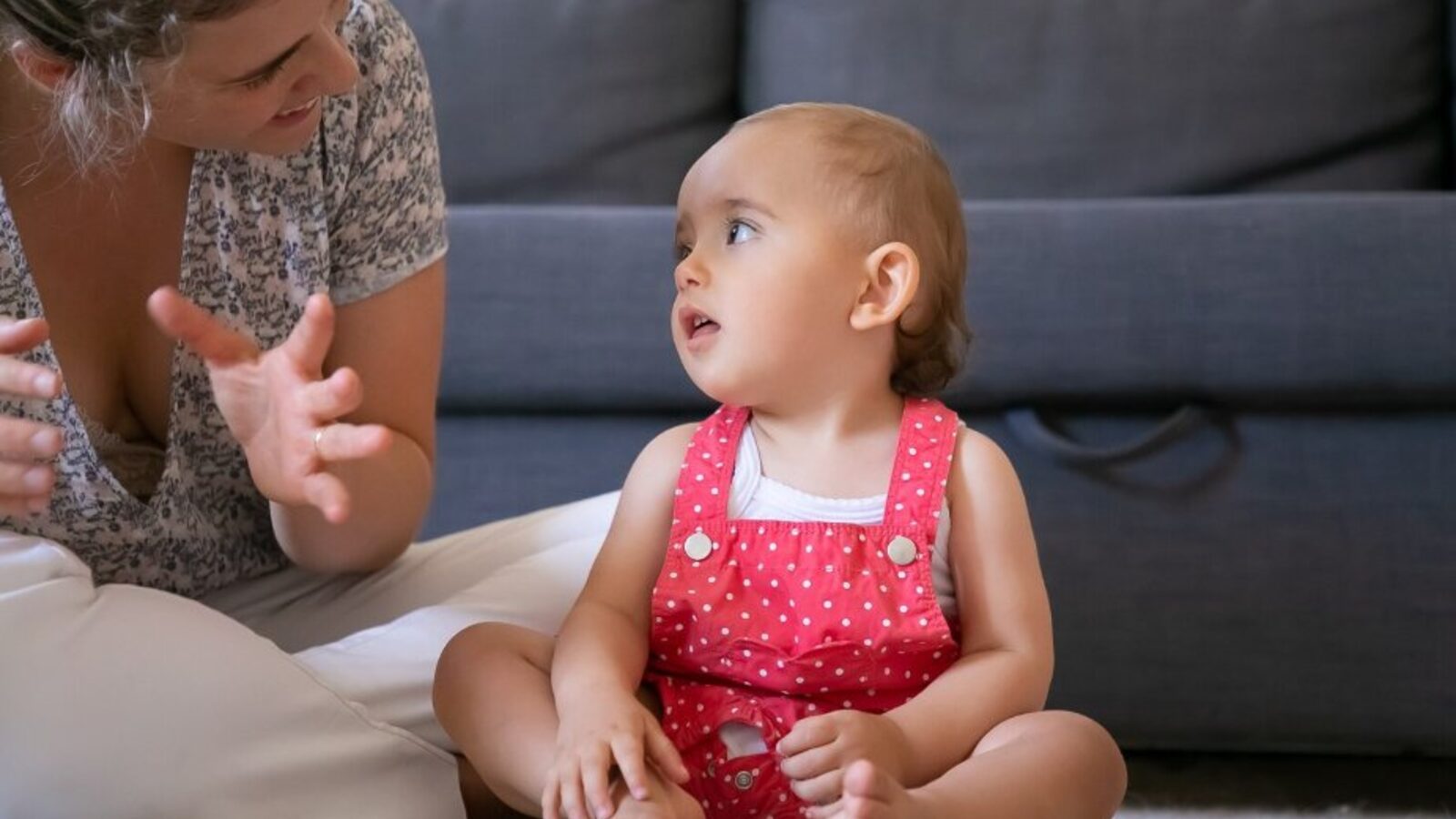 A parent sitting on the floor face-to-face with a baby, gesturing as they talk