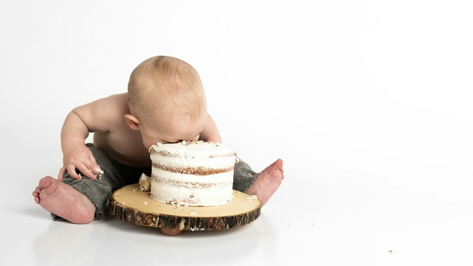 A baby exploring a small birthday cake on a wooden board